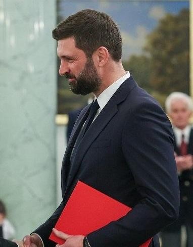 Nikodem Rachoń w trakcie prezentacji lub spotkania w formalnym otoczeniu, symbolizujący jego rolę w polityce międzynarodowej.