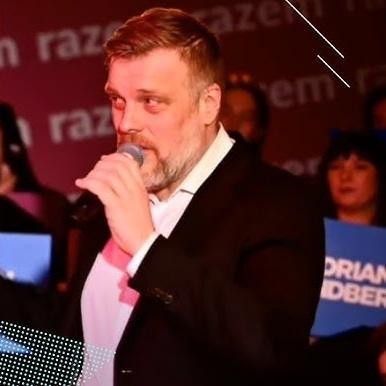 Adrian Zandberg wygłaszający przemówienie z mównicy, z widownią w tle, gestykulujący, co podkreśla jego zaangażowanie i pozycję lidera.