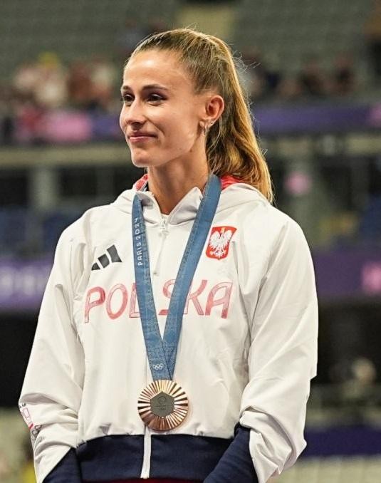 Natalia Bukowiecka celebrująca zwycięstwo na bieżni, z podniesionymi rękami, na tle stadionu.