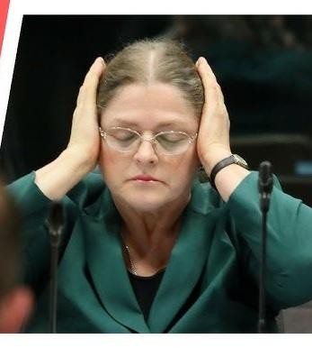 Krystyna Pawłowicz w trakcie wystąpienia publicznego lub posiedzenia, ukazana w dynamicznej pozie, oddającej jej zaangażowanie i stanowczość.