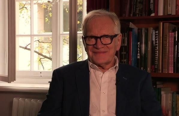 Andrzej Seweryn na scenie teatralnej, w dynamicznej pozie, oświetlony dramatycznym światłem scenicznym, oddający intensywność i pasję aktorskiego występu.
