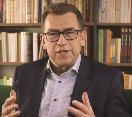 Maciej Orłoś podczas wystąpienia publicznego lub prowadzenia szkolenia, z mikrofonem, podkreślający jego doświadczenie i charyzmę.