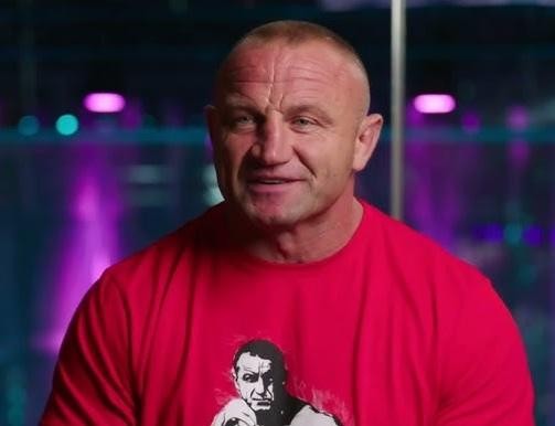 Mariusz Pudzianowski w oktagonie MMA, w rękawicach i spodenkach do walki, w tle ring KSW.