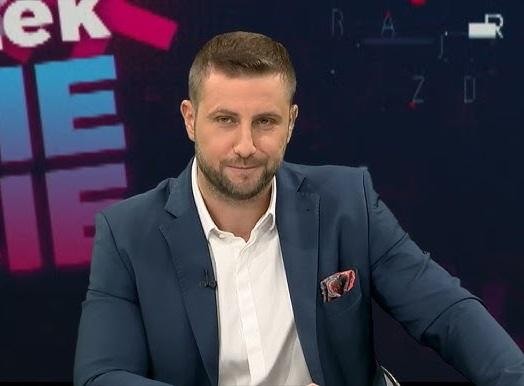 Studio telewizyjne podczas dynamicznej audycji na żywo, z widocznym stołem reporterskim i ekranami w tle.